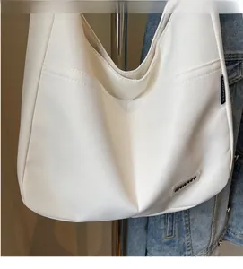 Detail of white canvas hobo bag showing front pocket and minimalist brand logo