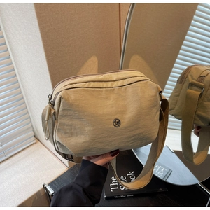 Détail du sac bandoulière beige en nylon imperméable avec logo métallique et sangle large