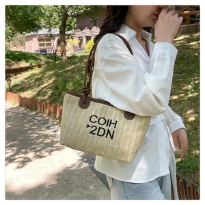 Outdoor close-up of a woven straw tote bag with brown leather straps and black embroidery
