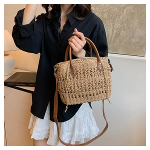 Detail of hollow-out straw handbag featuring brown PU handles and adjustable shoulder strap