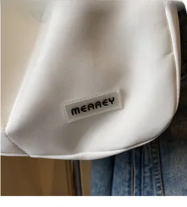 Detail of white canvas shoulder bag featuring a silicone logo tag and neat stitching