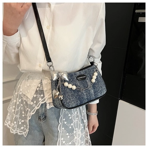 Détail d'un sac porté épaule en jean bleu avec nœuds métalliques et chaînes de perles