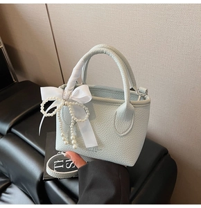 Detail of light blue bucket bag with lychee grain leather, pearl chain and silk ribbon