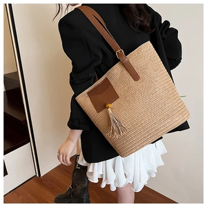 Detail of straw woven tote bag with brown leather patch and tassel on model shoulder