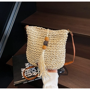 Dettaglio della borsa a secchiello in paglia beige con perline in legno e lunghe frange