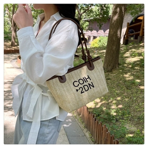 Outdoor shot showing the stylish woven straw tote bag texture and brown leather strap detail