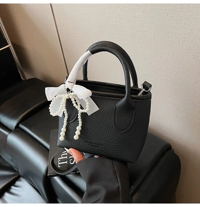 Close-up of black litchi pattern bucket bag with white ribbon and pearl bow charms