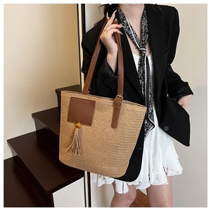 Detail of hand-woven straw tote bag with brown leather straps and decorative tassel