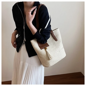Close-up of straw woven tote bag featuring brown leather straps and decorative tassel detail