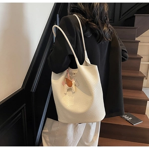 Detailed view of white woven tote bag with horse charm on a model in a minimal setting
