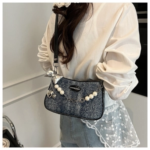 Detail of denim tweed bag featuring silver bow charm and pearl metallic chain strap