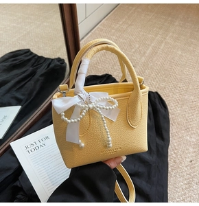 Detail of yellow lychee pattern leather bucket bag with pearl pendant and ribbon bow tie