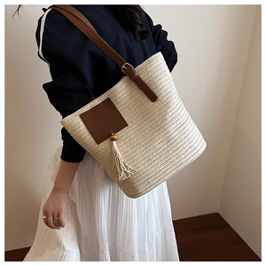Detail of a woven straw tote bag featuring leather shoulder strap and a boho tassel charm