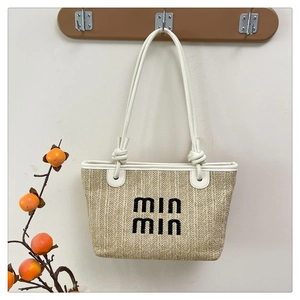 Detail of woven straw tote bag featuring white leather handles and min min embroidery