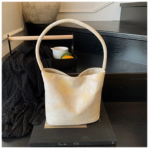 Detail of floral patterned beige tote bag with a cylindrical handle in a lifestyle setting