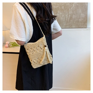 Detailed close-up of handmade woven straw bucket bag with floral patterns and tassels