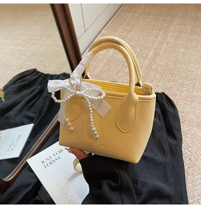 Detail of yellow litchi grain bucket bag with pearl bow ribbon and branded logo