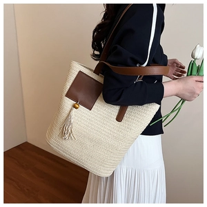 Detail of woven straw tote bag featuring brown leather patch and wood bead tassel decoration