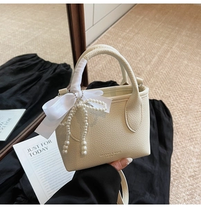 Detail of off-white mini bucket bag with lychee texture and elegant pearl strap charm