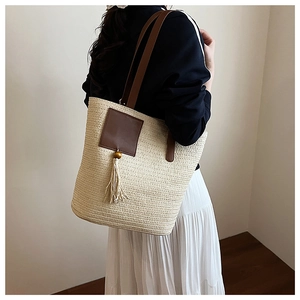 Detail of handwoven beige straw tote bag featuring leather patch and tassel with wood beads