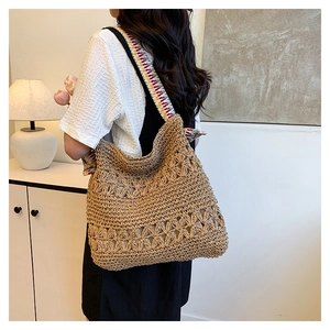Detail of hand-woven straw tote bag with floral patterns and colorful shoulder strap