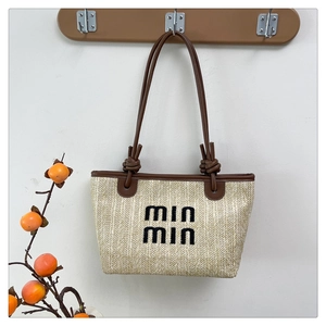 Detail of woven straw tote bag with brown leather trim and Min Min embroidery