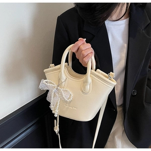 Detail of a beige mini bucket bag with lace pearl bow charm and embossed logo on faux leather