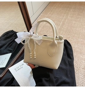 Detail of off-white lychee grain leather handbag with pearl bow charm and brand logo