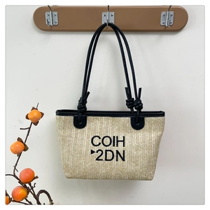 Close-up of woven straw tote bag with black leather straps and COIH 2DN embroidery