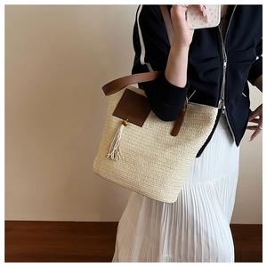 Detail of summer straw tote bag featuring brown leather patch, fringe, and shoulder straps