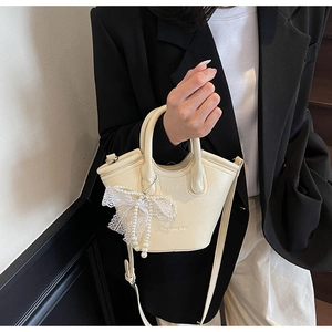 Detail of cream white textured mini bucket bag with pearl lace bow charm on a model