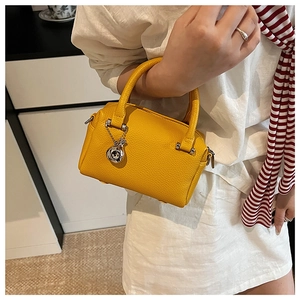 Détail d'un sac Boston jaune vif en cuir grainé avec un pendentif sphérique argenté
