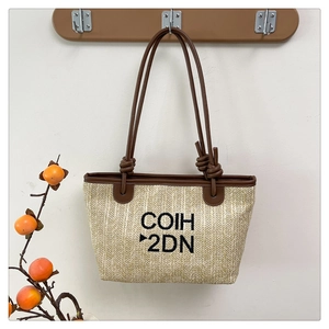 Detail of woven straw tote bag with black COIH 2DN embroidery and brown knot handles