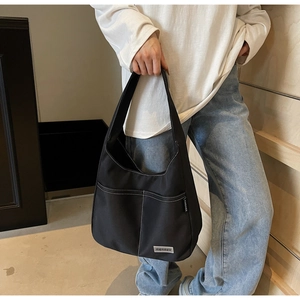 Close-up of black canvas shoulder bag featuring contrast white stitching and textile label