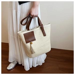 Detail of woven straw tote bag with brown leather handles and wooden bead tassels