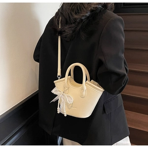 Close-up of cream mini tote bag with pearl lace bow detail on a black blazer background