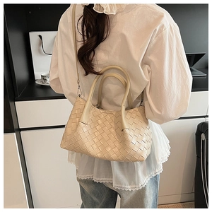 Détail du sac seau en cuir tressé beige porté par le mannequin avec bandoulière amovible