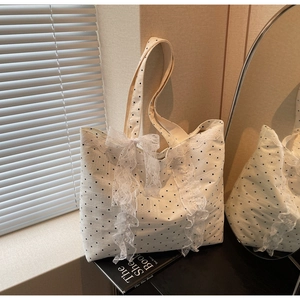 Détail du sac cabas blanc à pois avec dentelle et nœud posé sur des livres noirs