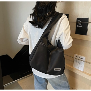 Detail view of black canvas hobo bag with white contrast stitching and metal brand logo