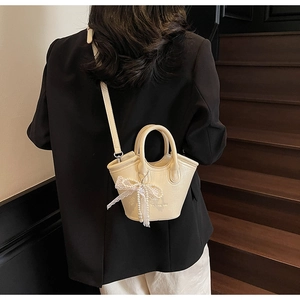 Detail of cream bucket bag with lace bow, pearl chain and brand logo on leather