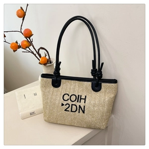 Detail of woven straw tote bag with black leather handles and COIH 2DN printed lettering