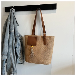 Detail of woven straw tote bag featuring brown leather patch and stylish beige tassel