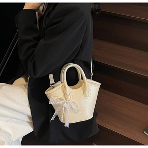 Detailed side view of a cream tote bag featuring a lace bow and pearl charm on stairs