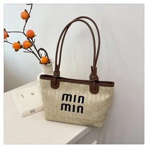Detail of woven straw tote bag featuring brown leather handles and min min embroidery
