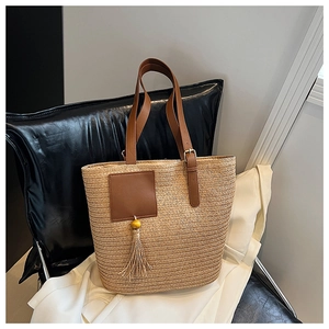 Detail of hand-woven straw tote bag featuring brown leather handles and fringe tassel