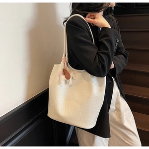 Detail of cream white tote bag with crocodile pattern and a pegasus charm on a model