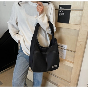 Detail of black tote bag featuring contrast white stitching and metal brand logo accent