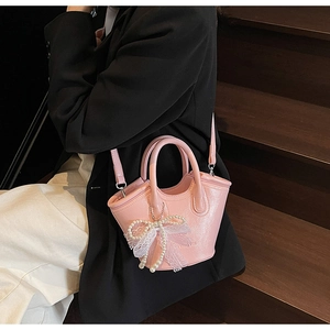 Detail view of pink bucket bag with pearl bow charm and leather finish on wooden steps