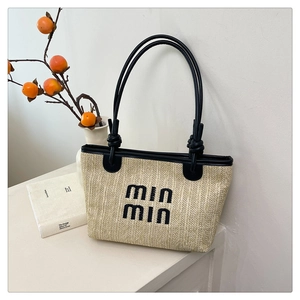 Detail of woven straw tote bag with black leather straps and embroidered logo
