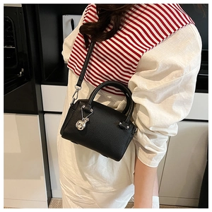 Gros plan du sac Boston en cuir grainé noir avec charme pomme argenté et bandoulière